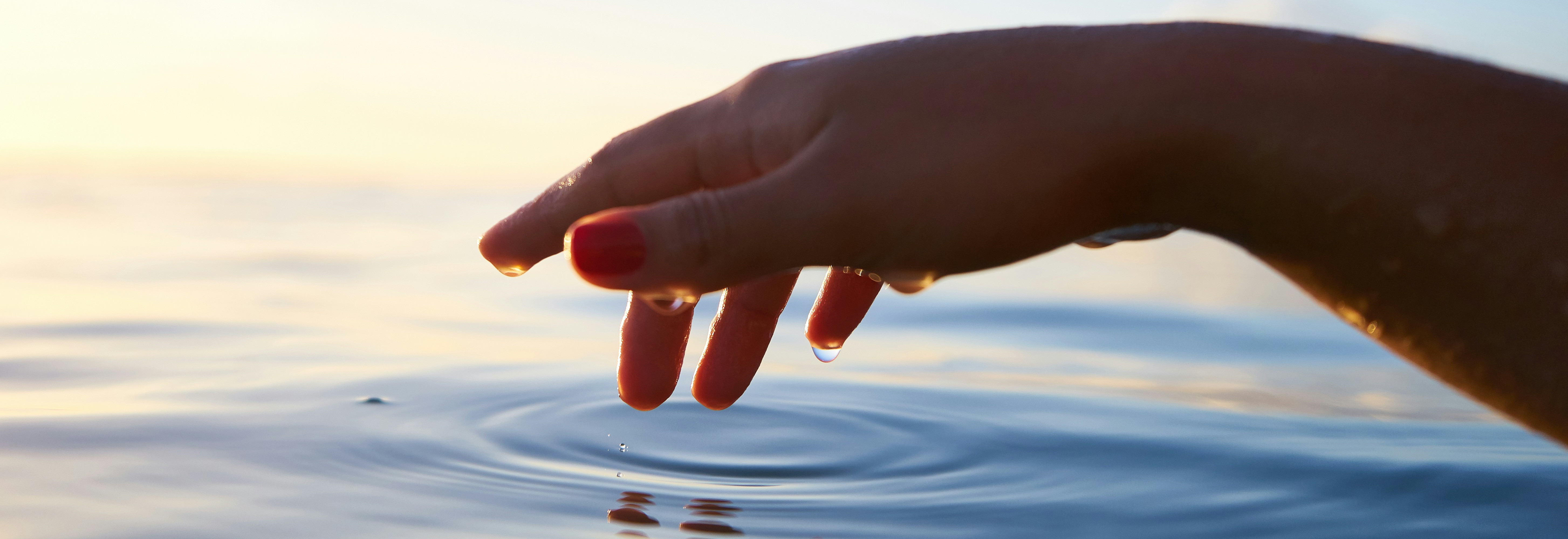 Hand touching water surface at sunset